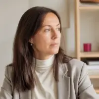 Portrait de Mathilde Marcenac, cheveux bruns mi-longs, blazer gris clair sur un col roulé écru, dans une pièce claire